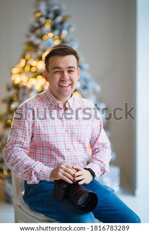 male photographer in a plaid shirt with a camera at the Christmas tree. traditional New year family photo sessions in the Studio. seasonal work. festive atmosphere.