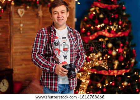 male photographer in a plaid shirt with a camera at the Christmas tree. traditional New year family photo sessions in the Studio. seasonal work. festive atmosphere.
