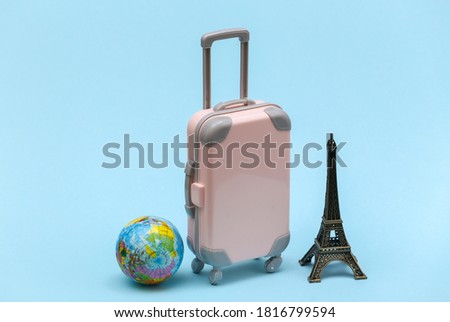 Traveled to Paris. Mini plastic travel suitcase and statuette of the Eiffel Tower, globe on blue background.