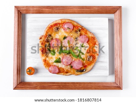 Homemade mini pizza with sausage, mushroom and cheese on the white board in the wooden picture frame. Imperfect food. Idea of the kitchen interior design