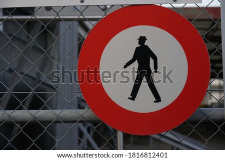 No entry or no access sign with a silhouettes of a person on a white circular ground with red circle around. The sign is placed on a fence of industrial ground. 