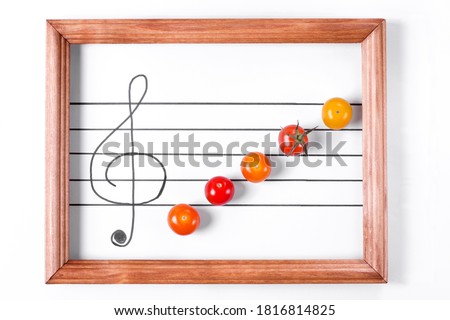 Multicolored cherry tomatoes on the musical staff in the wooden frame. Creative food background. Symphony of flavors. Idea of the kitchen interior design