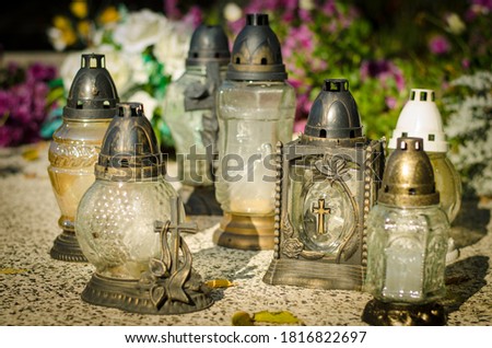 burning candles in lanterns in the grave with colorful autumnal atmosphere during sunny afternoon