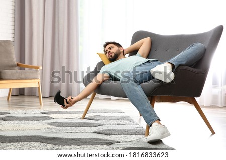 Lazy young man playing video game while lying on sofa at home