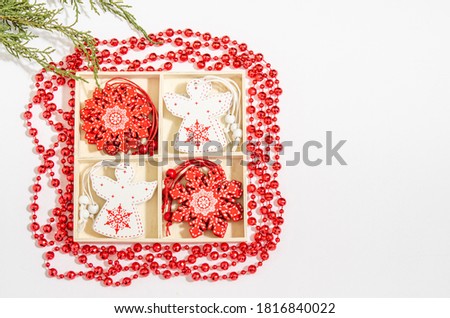Christmas wooden toys white angel and red snowflake in a wooden box, red beads, juniper branches on a white background. Space for copy space, flat lay. View from above