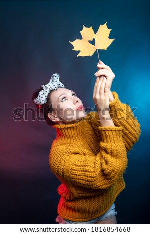 A woman in a yellow sweater holds a maple leaf above her with a cut out heart, studio photo, dark background