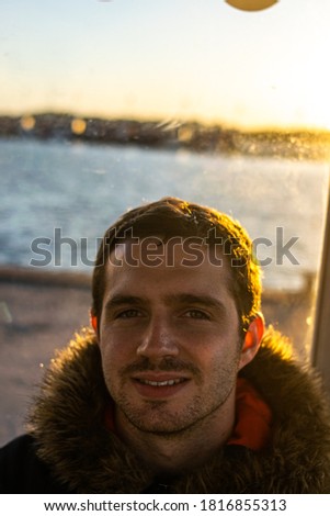 Photo of a young and attractive man wearing a winter jacket smiling and with the beach at the horizon. Portrait of guy with beard