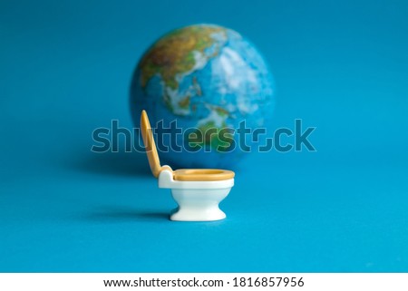 White toilet with an orange lid on a blue background with a globe in honor of world toilet day 19 November which is dedicated to public toilets and their maintenance, focus in the foreground Royalty-Free Stock Photo #1816857956