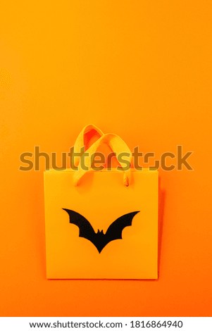Empty orange paper bag with hand carved silhouette of black bat on bright orange paper background. Vertical background with large copy space. Zero waste and plastic free Halloween concepts.