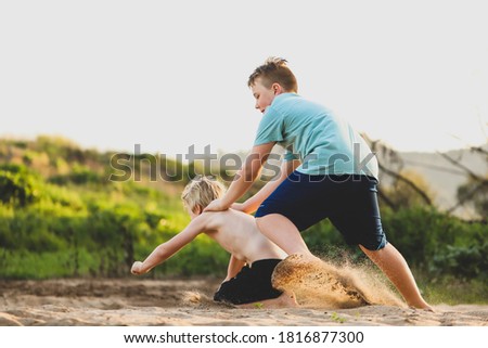 Young boys wrestling in sand causing dust on river bed at sunset