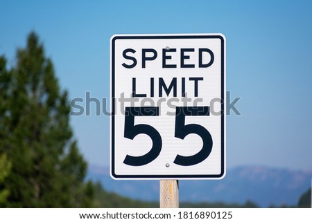 Fifty-five mph speed limit sign on highway. Speed zone traffic sign against blurred tree landscape and blue sky.