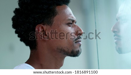 Pensive black man looking out home window