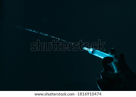 Hand of anonymous person using syringe with water drops against dark background.