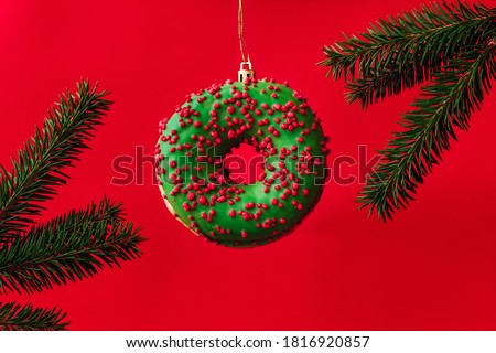 Christmas composition of green donut in the form of a New Year toy and tree branches on a red background. Celebration, food art, holiday concept.