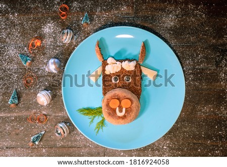 Funny food with edible symbol of 2021 bull cow made from bread, cheese and vegetables. Breakfast idea for kids. New Year Christmas food top view. Holiday, celebration, art food. 