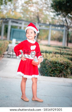 little asian girl in red Santa Claus costume with present box in the park