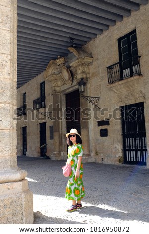 An Asian female tourist with colorful dress standing in front of a classic style building in Plaza de Armas in old town Havana.