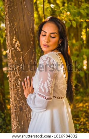 A closeup portrait of a beautiful young Hispanic female in white dress posing at the camera in nature