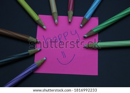 An image of color pencils and sticky note with word happy on it. isolated on black background.