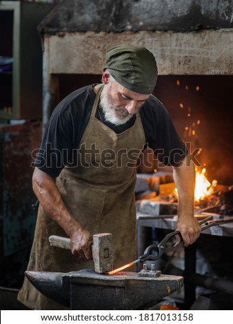 Old blacksmith working metal with hammer on the anvil in the forge Royalty-Free Stock Photo #1817013158