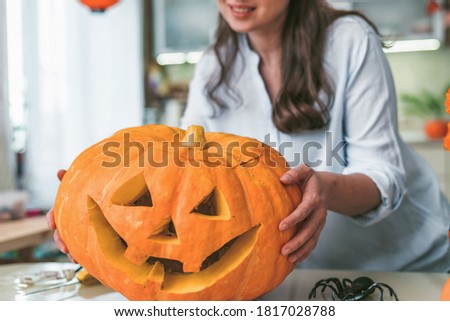 woman holding pumpkin or pumpkin lantern at home in kitchen. carved pumpkins in jack lanterns for Halloween, decorations and festive concepts. Helloween concept. Close up.