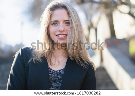 Young woman, blonde, European descent. Woman posing in a black jacket, on the stairs of concrete in a city park. Woman about 21 years. Photo taken in the cold season
