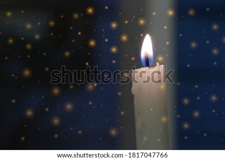 white candle flame is surrounded by bright sparks in the dark blue background. Christmas and New year concept. 