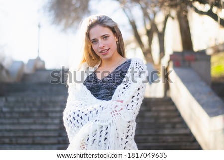 Young woman, blonde, European descent. A woman poses wrapped in a large, white lace shawl on a concrete staircase in a city park. The woman is about 21 years old. Photo taken during the cold season