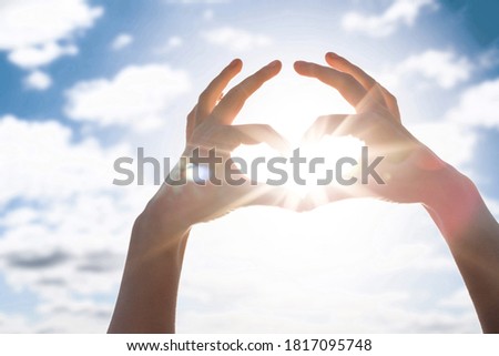 Heart of the fingers against the blue sky and sun