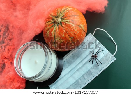 Pumpkin, spider web, spider, candle and medical mask on a dark green background. The concept of celebrating Halloween in 2020 is associated with the threat of the spread of the covid-19 virus