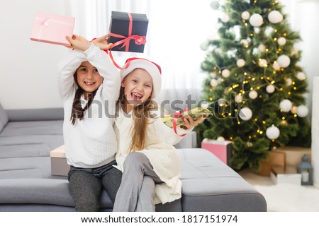 Two little girls in the Santa hat open Christmas present under the Christmas tree