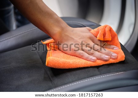 Man's hand cleaning car interior in luxury car with microfiber cloth. Hand wipe down suede leather seat of sports sedan.  Interior car detail & leather seat repair background. Car wash & clean concept Royalty-Free Stock Photo #1817157263