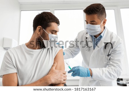 medicine, vaccination and healthcare concept - doctor wearing face protective medical mask for protection from virus disease with syringe doing injection of vaccine to male patient Royalty-Free Stock Photo #1817163167