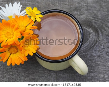 Medical herb chamomile and calendula with yellow and orange flowers and herbal tea in an enameled mug on a wooden stand, top view. Useful plant marigold for use medicine, homeopathy and cosmetology