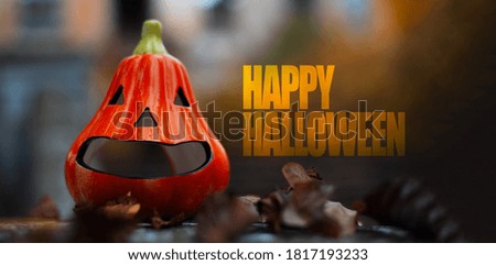 Close-up of Happy Halloween text and orange pumpkin, on blurred outdoors background.