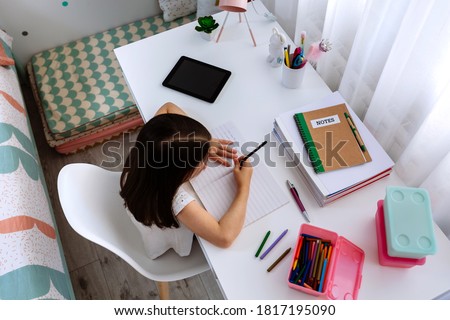 Top view of unrecognizable girl doing homework sitting at a desk in her bedroom Royalty-Free Stock Photo #1817195090