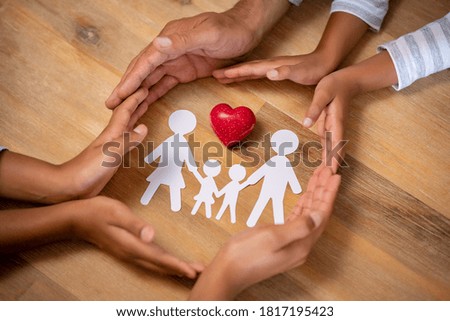 Close up hands of father, mother and daughters protecting family paper cutout with red heart. Hands of family with paper cutting and red heart shaped symbol stone. Unity, insurance and love concept.