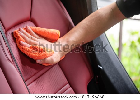 Man's hand cleaning red interior in luxury car with microfiber cloth. Hand wipe down leather seat of sports car.  Interior car detail and leather seat repair & cleaning background. Car wash concept. Royalty-Free Stock Photo #1817196668