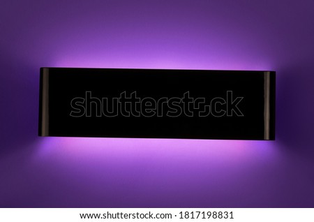 A glowing modern black led lamp on the dark purple wall.