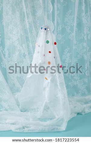 Lace curtain ghost made with a disco ball covered with multicolored flowers on the sheet. Blue background. Offbeat humor and pop atmosphere. minimal color still life photography 