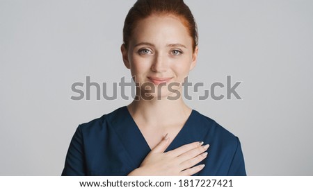 Attractive smiling doctor holding hand on heart dreamily looking in camera isolated. Tender and touched expression