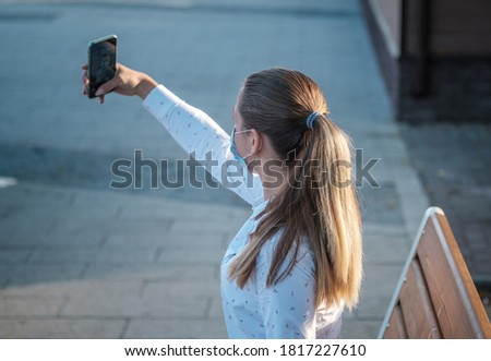 a young lady in a medical mask takes a selfie with her smartphone. concept of quarantine, mask mode during the covid-19 pandemic