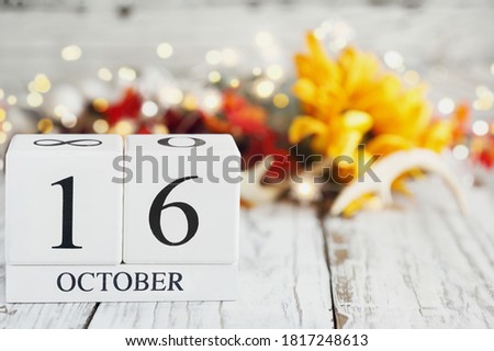 White wood calendar blocks with the date October 16th and autumn decorations over a wooden table. Selective focus with blurred background. 