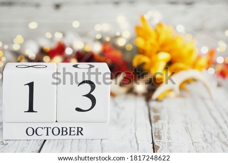 White wood calendar blocks with the date October 13th and autumn decorations over a wooden table. Selective focus with blurred background. 