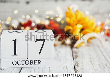 White wood calendar blocks with the date October 17th and autumn decorations over a wooden table. Selective focus with blurred background. 