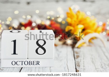 White wood calendar blocks with the date October 18th and autumn decorations over a wooden table. Selective focus with blurred background. 