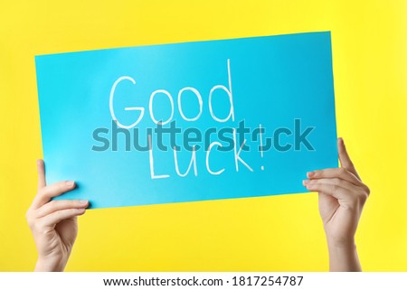 Woman holding light blue card with words GOOD LUCK on yellow background, closeup