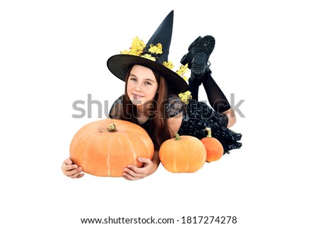 Cute girl with black hat on her head lying on his stomach on a white background including pumpkins on Halloween, picture with depth of field.
