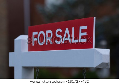 New red sign for sale in front of house in residential area. Real estate bubble, bidding war, hot housing market, overpriced property, buyer activity, spring and summer sale  concept. Selective focus.