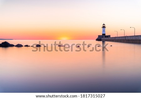 Calm water, lighthouse and reflections at sunrise in Duluth, MN Royalty-Free Stock Photo #1817315027